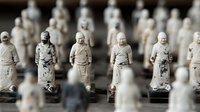 Rows of small white ceramic monk figurines with weathered patina and traditional robes create repetitive pattern in shallow depth of field composition.