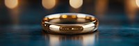 Golden wedding ring on dark blue wooden surface with soft bokeh lights in background, romantic minimalist jewelry composition for marriage proposal.