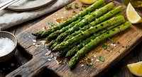 Fresh grilled asparagus spears on wooden cutting board with herbs, lemon and sea salt. Healthy green vegetable side dish for cooking and meal preparation.