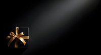 Black gift box with golden ribbon bow on dark background, suitable for holiday, celebration, and luxury product marketing materials.