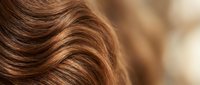 Close-up of shiny brown hair with golden highlights showing smooth wavy texture and natural shine for beauty and haircare concepts.