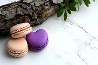 French macarons in peach and purple shades on marble surface with rustic wood bark and green leaves, creating elegant food composition for bakery marketing.