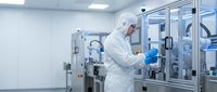Male scientist in protective suit working with laboratory equipment in sterile pharmaceutical manufacturing facility for drug development and quality control.