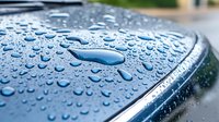 Water droplets and rain beads on metallic blue car surface showing hydrophobic coating effect, macro photography with selective focus and bokeh background.