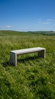 Wooden bench placed in lush green meadow with rolling hills and clear blue sky, suitable for outdoor furniture marketing and landscape design projects.