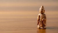 Wooden figurine of Asian warrior in traditional robes standing on smooth surface against warm blurred background for meditation and mindfulness concepts.
