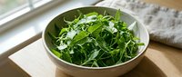 Fresh mixed green salad with arugula and leafy vegetables in white bowl on wooden surface, ready for healthy eating.