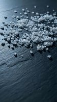 Sea salt crystals scattered on dark slate surface, close-up macro shot with shallow depth of field. Use for culinary, food styling, seasoning, gourmet cooking, and ingredient photography.
