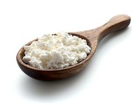 Fresh cottage cheese in wooden spoon isolated on white background. Natural dairy product with grainy texture for healthy eating and cooking.
