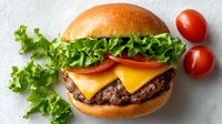 Fresh beef cheeseburger with lettuce and tomato on sesame bun, served with cherry tomatoes on white background for restaurant menu design.