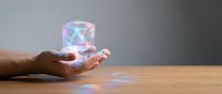 Hand holding glowing holographic cube with colorful light projections on wooden surface, representing technology, innovation, and digital transformation concepts.
