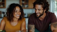 Happy mixed race couple laughing together in modern kitchen during casual conversation at home creating warm intimate domestic atmosphere.