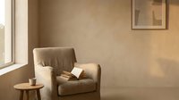 Cozy reading nook with beige armchair, wooden side table, and natural light from window in minimalist interior design space.