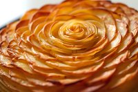 Golden apple rose tart with caramelized fruit slices arranged in spiral pattern on pastry base for bakery menu and dessert photography.