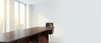 Modern minimalist office interior with wooden desk and black chair near large windows with natural sunlight streaming in creating bright workspace.