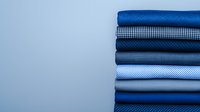Stack of neatly folded blue and white textile fabrics with different patterns and textures arranged in gradient order against light background for fashion design.