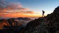 Silhouette of male hiker running on rocky mountain ridge at golden sunset with misty valleys below, adventure and outdoor fitness concept for trail running and mountaineering.