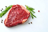Raw ribeye steak with fresh rosemary sprigs and scattered peppercorns on white background, marbled red meat texture showing premium beef quality.