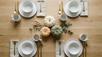 Autumn table setting with white plates, pumpkins and eucalyptus on wooden background for Thanksgiving dinner celebration and fall dining decor.