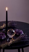 Mystical altar setup with burning black candle, crystal ball, amethyst stones and dried lavender bundles on dark marble table for spiritual practices.