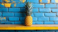 Fresh pineapple on yellow wooden shelf against bright blue brick wall with peeling paint, creating vibrant tropical urban contrast. Modern food photography.