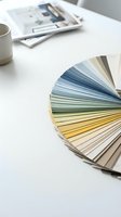 Color palette fan deck samples on white desk with coffee cup and magazines for interior design and home renovation planning projects.