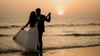 Romantic wedding couple silhouette dancing on beach at sunset with golden ocean waves creating intimate moment for celebration and love concept.