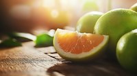 Fresh ripe green grapefruit sliced on rustic wooden table with warm sunlight and bokeh effect, natural organic citrus fruit composition.