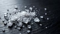 White coarse sea salt crystals scattered on dark wooden surface for cooking and culinary seasoning applications in kitchen and food preparation.