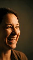 Joyful middle-aged Asian woman laughing heartily with genuine happiness, warm lighting creating dramatic shadows on face for emotional wellness content.