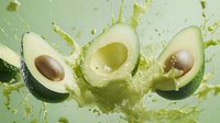 Fresh avocado halves with splashing juice on light green background, showcasing ripe fruit with pits for healthy eating and food preparation.