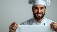 Middle Eastern male chef with beard wearing white uniform and toque holds blank white banner against gray background, smiling confidently at camera.