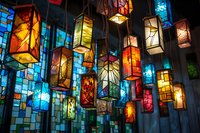 Colorful stained glass lanterns hanging from ceiling, illuminated with vibrant reds, blues, yellows creating magical atmosphere for festive decoration.