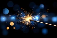 Bright sparkler emitting golden sparks against dark background with blue and orange bokeh lights creating magical festive atmosphere for celebration designs.