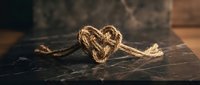 Heart-shaped rope knot on dark wooden surface symbolizing love, connection and unity for romantic designs and crafts.