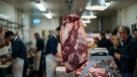 Whole raw beef carcass hanging in butcher shop with workers processing meat in background, suitable for food industry, culinary, and restaurant marketing.