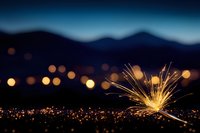 Bright sparkler against dark mountain silhouette with glowing city lights bokeh in background creates magical nighttime atmosphere. Perfect for holiday celebrations.