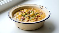 Creamy potato soup with bacon bits and herbs served in rustic enamel bowl on white wooden table for comfort food recipes and cooking blogs.