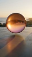 Reflective copper sphere on concrete surface with golden sunset and ocean backdrop, casting warm shadows for artistic and conceptual design projects.