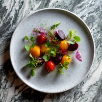 Fresh colorful heirloom tomatoes and beets garnished with microgreens and edible flowers on gray ceramic plate against marble background, fine dining presentation.