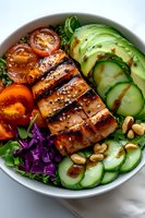 Grilled teriyaki salmon bowl with fresh avocado, cucumber slices, cherry tomatoes, purple cabbage, and mixed greens topped with sesame seeds and peanuts on marble surface.