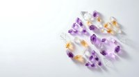 Colorful transparent capsules with purple and orange pills scattered on white background for pharmaceutical and healthcare design projects.