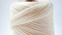 White cotton thread spool macro view showing detailed fiber texture and winding pattern on wooden core, suitable for crafting, sewing and textile design projects.