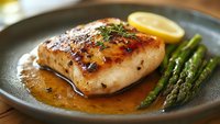 Grilled chicken breast with honey glaze sauce served on gray ceramic plate with fresh asparagus and lemon slice, close up view of gourmet dinner meal.