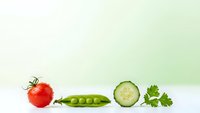 Fresh organic vegetables including red tomato, green peas in pod, cucumber slice and parsley herbs arranged in row on clean white surface.