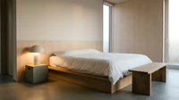 Modern minimalist bedroom with wooden bed frame and white bedding in contemporary apartment interior for home design and real estate concepts.