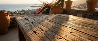 Wooden table on terrace overlooking coastal landscape at golden hour, with potted flowers and Mediterranean scenery, suitable for travel and lifestyle design.
