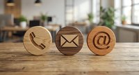 Three wooden contact icons on office desk showing phone, email and at symbol for business communication and customer service concepts.