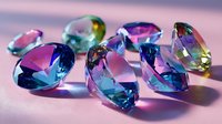 Colorful crystal gemstones with blue, pink, and yellow facets scattered on pink surface, creating prismatic light reflections for jewelry design inspiration.