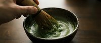 Matcha tea preparation with whisk blending powdered green tea in ceramic bowl for traditional Japanese ceremony or wellness beverage making.
